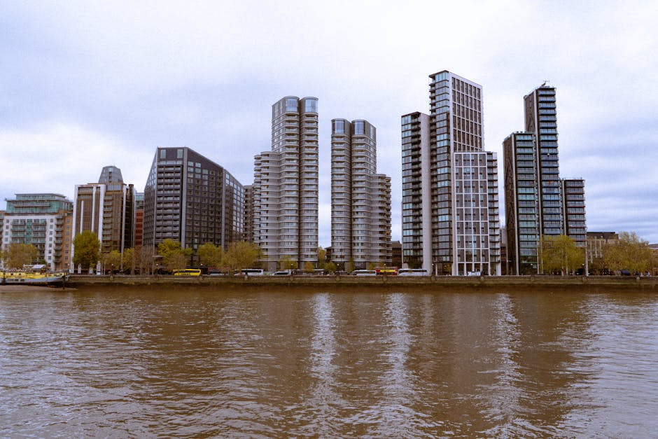 A nighttime cityscape of London’s South Bank showing modern office buildings and the distinctive Shard skyscraper illuminated in purple light. The buildings are situated along the riverbank, with their glass facades reflecting in the calm water below. The sky overhead is filled with purple-tinged clouds, creating a dramatic backdrop. In the foreground, the river’s surface appears gently rippled, with reflections of the illuminated windows and city lights. This scene captures the vibrant urban environment characteristic of London’s riverside, relevant to home relocation and furniture transport services such as those provided by Lambeth Movers, especially during the loading process of a house removal along the South Bank.